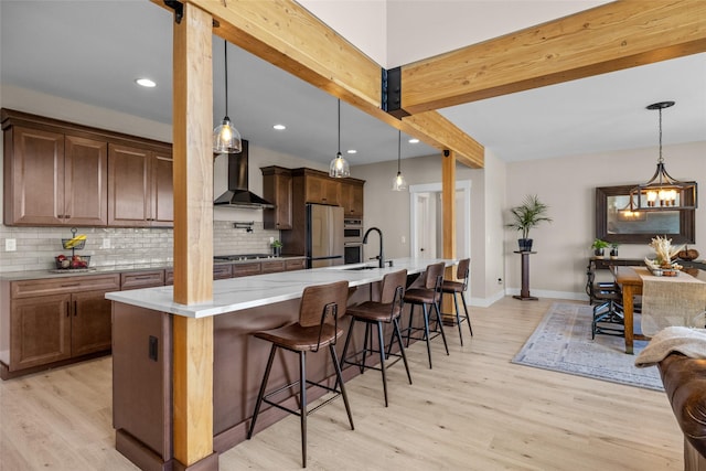 kitchen featuring a kitchen breakfast bar, wall chimney range hood, beam ceiling, pendant lighting, and fridge