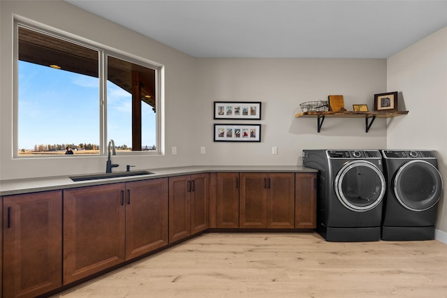 clothes washing area with cabinets, light wood-type flooring, separate washer and dryer, and sink