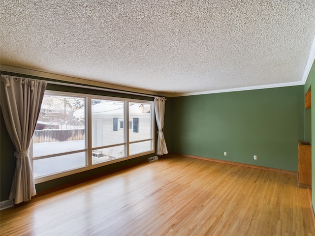 empty room featuring a textured ceiling, hardwood / wood-style flooring, a wealth of natural light, and crown molding