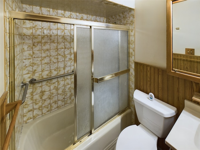 full bathroom with wooden walls, vanity, enclosed tub / shower combo, and toilet