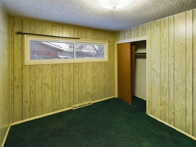 unfurnished bedroom with dark colored carpet, a textured ceiling, a closet, and wood walls