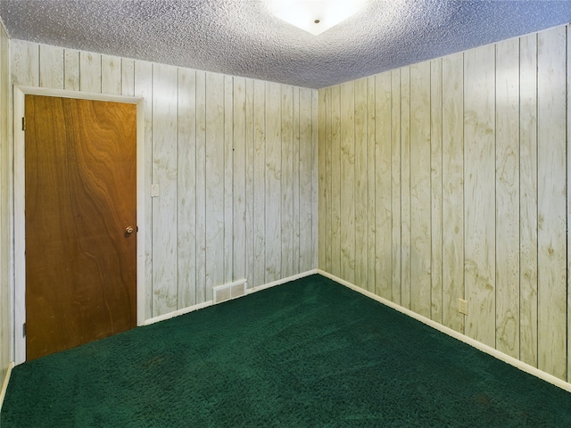 empty room featuring dark colored carpet, a textured ceiling, and wooden walls