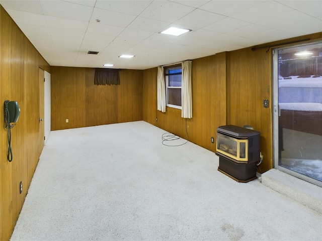 basement with a wood stove, wooden walls, and light colored carpet