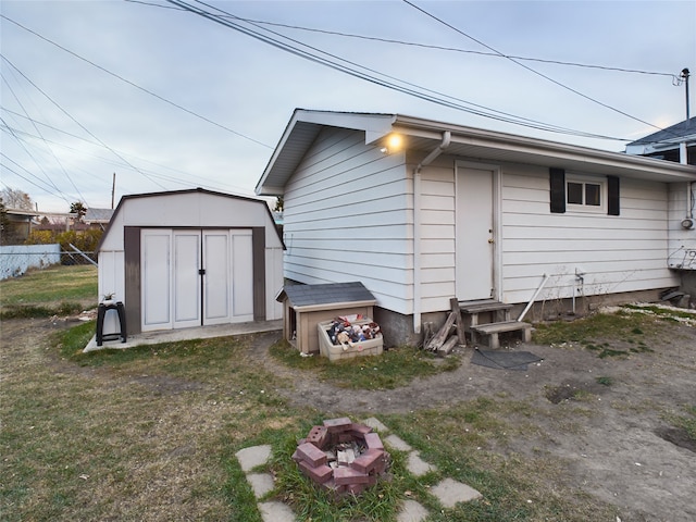 back of property featuring a fire pit, a storage unit, and a lawn