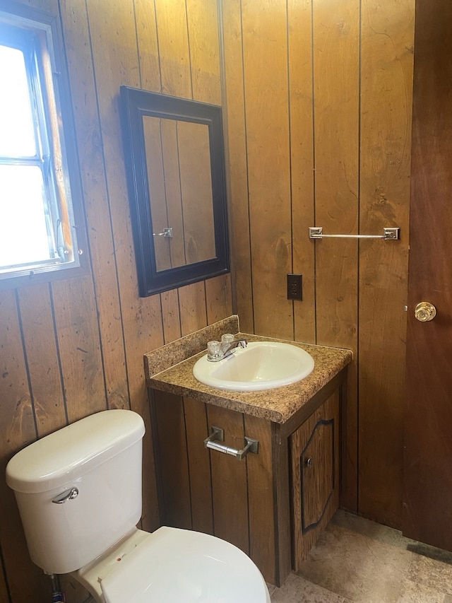 bathroom with wooden walls, vanity, a healthy amount of sunlight, and toilet