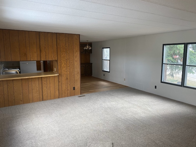 unfurnished living room with a notable chandelier, light carpet, and wooden walls