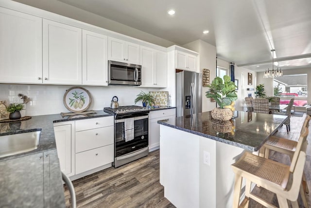 kitchen with a kitchen breakfast bar, stainless steel appliances, dark wood-type flooring, white cabinetry, and a kitchen island