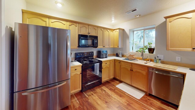 kitchen with sink, light brown cabinets, black appliances, and light hardwood / wood-style flooring