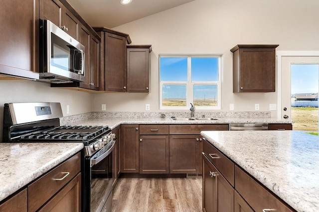 kitchen featuring appliances with stainless steel finishes, dark brown cabinets, vaulted ceiling, sink, and hardwood / wood-style floors