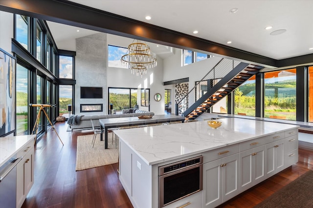 kitchen featuring light stone countertops, stainless steel oven, a kitchen island, white cabinetry, and hanging light fixtures