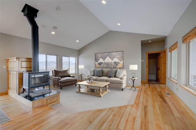 living room featuring a wood stove, high vaulted ceiling, and light hardwood / wood-style flooring