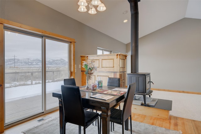 dining area featuring a wood stove, a mountain view, a chandelier, wood-type flooring, and vaulted ceiling