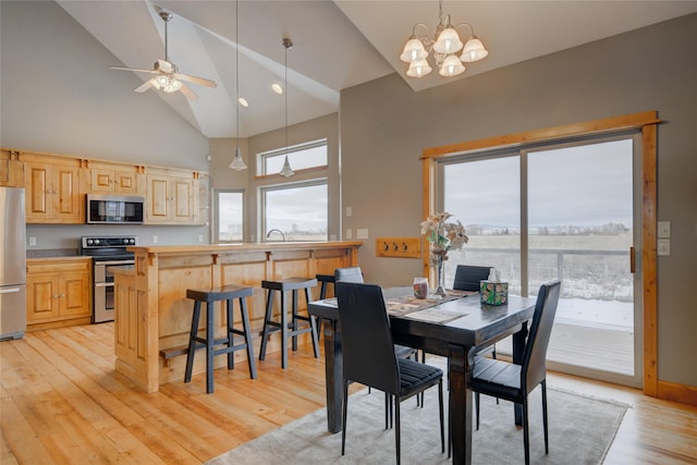 dining space with ceiling fan with notable chandelier, light hardwood / wood-style floors, and high vaulted ceiling