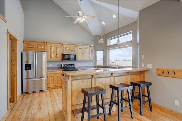 kitchen with light brown cabinets, a kitchen breakfast bar, high vaulted ceiling, kitchen peninsula, and appliances with stainless steel finishes