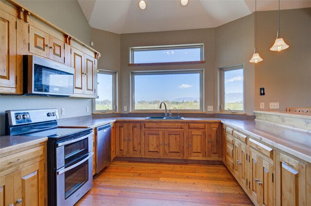 kitchen featuring pendant lighting, lofted ceiling, sink, light hardwood / wood-style flooring, and stainless steel appliances