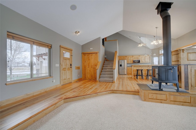 living room featuring ceiling fan with notable chandelier, a wood stove, carpet floors, and lofted ceiling