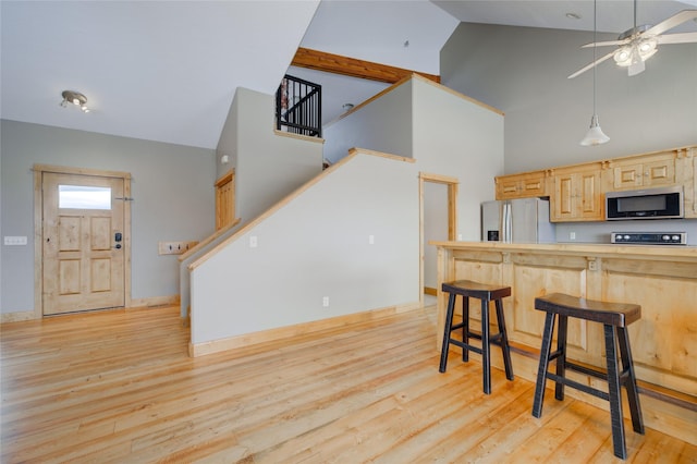 kitchen featuring light brown cabinets, high vaulted ceiling, appliances with stainless steel finishes, light hardwood / wood-style floors, and a breakfast bar area