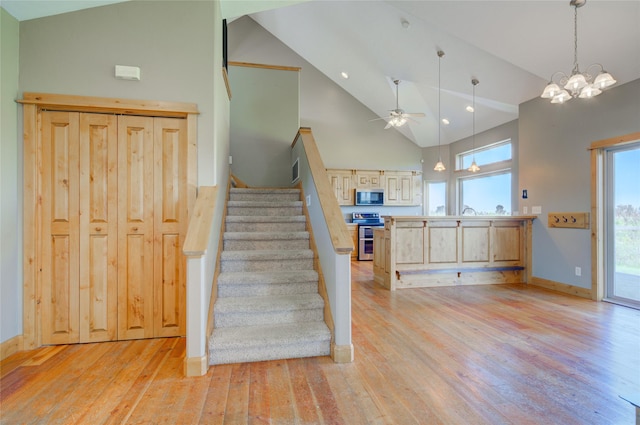 stairway with hardwood / wood-style floors, high vaulted ceiling, and ceiling fan with notable chandelier