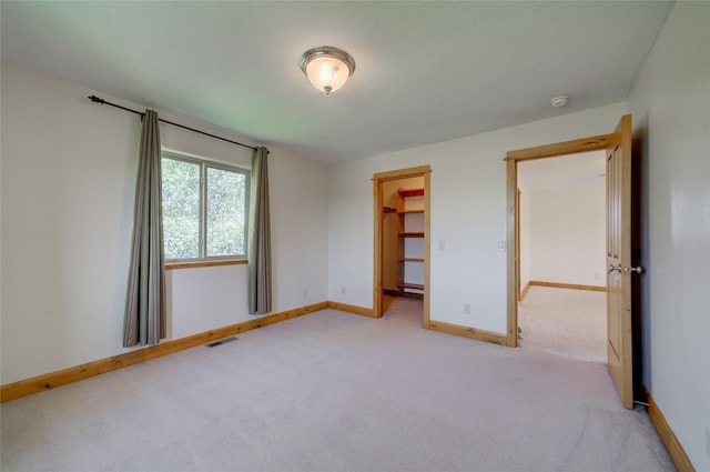 unfurnished bedroom with a walk in closet, light carpet, and a closet