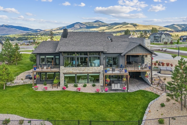 rear view of property featuring a mountain view, a balcony, and a lawn