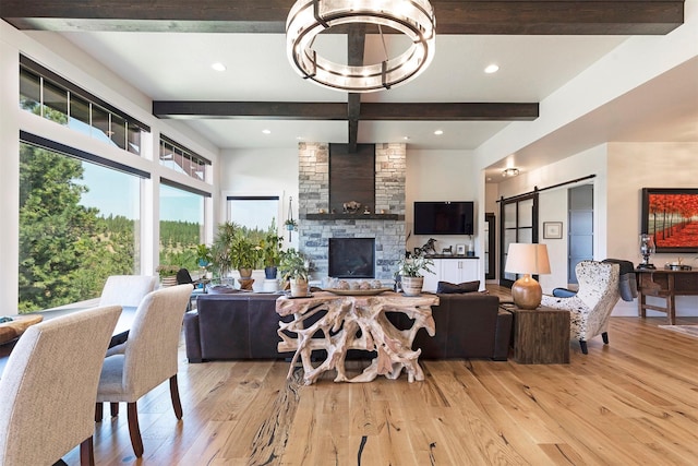 living room featuring a barn door, a stone fireplace, beamed ceiling, and light hardwood / wood-style flooring