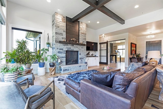 living room featuring beam ceiling, a barn door, a notable chandelier, a fireplace, and light wood-type flooring