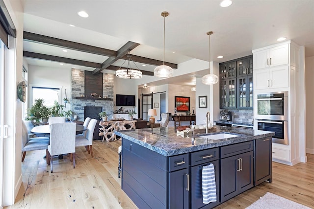 kitchen with beam ceiling, light hardwood / wood-style floors, an island with sink, and double oven