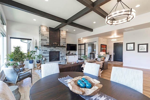 dining area featuring beamed ceiling, a fireplace, light hardwood / wood-style flooring, and a chandelier