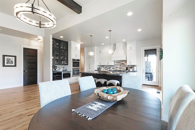 dining room featuring beam ceiling, light hardwood / wood-style flooring, and a chandelier