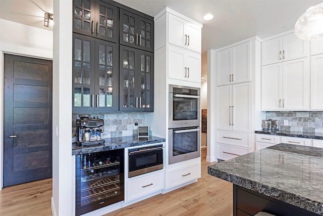 kitchen with stainless steel double oven, wine cooler, backsplash, dark stone counters, and white cabinets