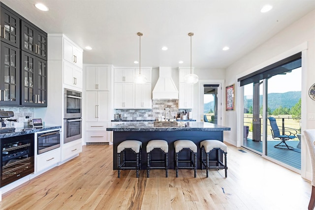 kitchen with white cabinets, decorative backsplash, stainless steel double oven, and custom exhaust hood