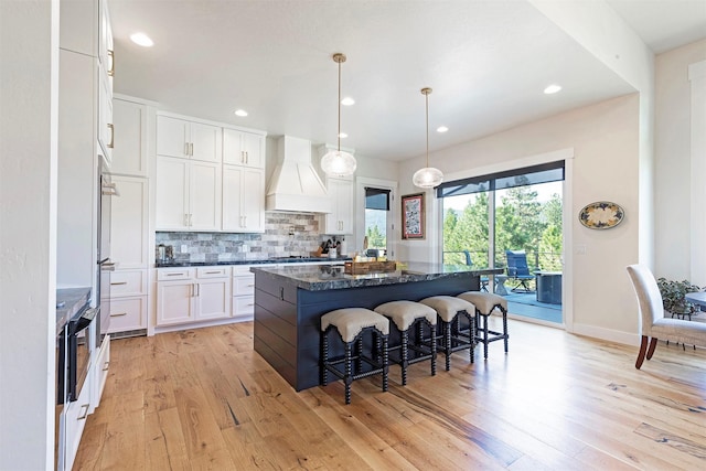 kitchen featuring backsplash, custom exhaust hood, white cabinetry, hanging light fixtures, and a breakfast bar area