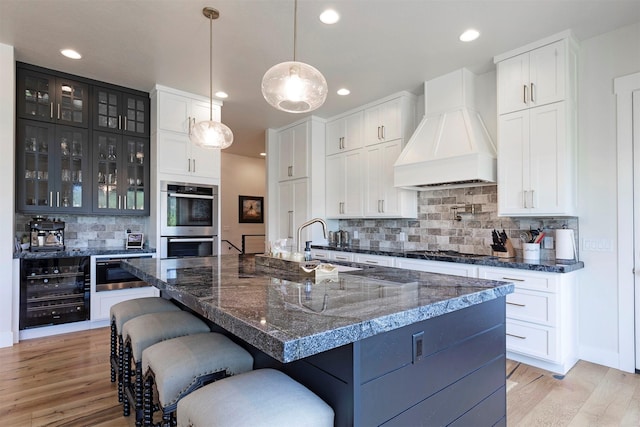 kitchen with a large island, stainless steel double oven, tasteful backsplash, decorative light fixtures, and custom exhaust hood