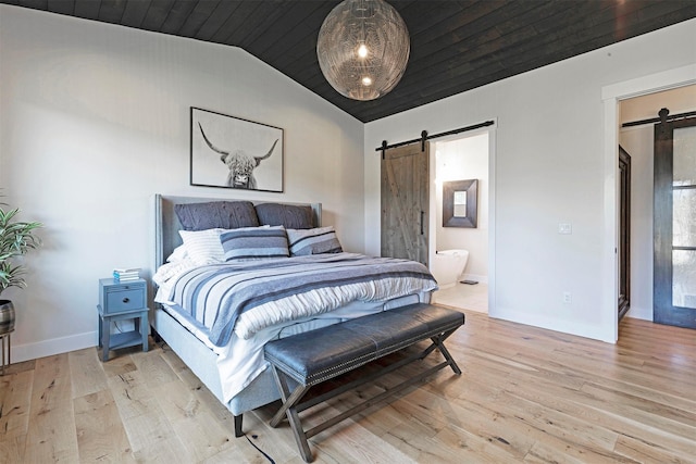 bedroom featuring a barn door, ensuite bathroom, and light hardwood / wood-style flooring