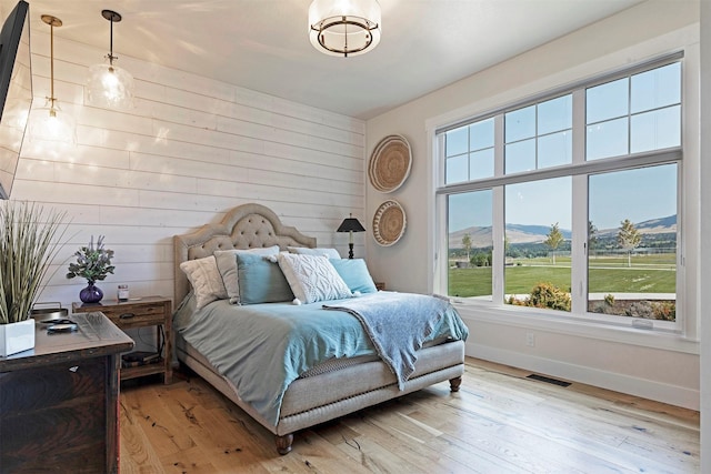 bedroom with a mountain view, light hardwood / wood-style floors, and wooden walls