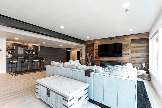 living room with bar area, light hardwood / wood-style floors, a wealth of natural light, and wood walls