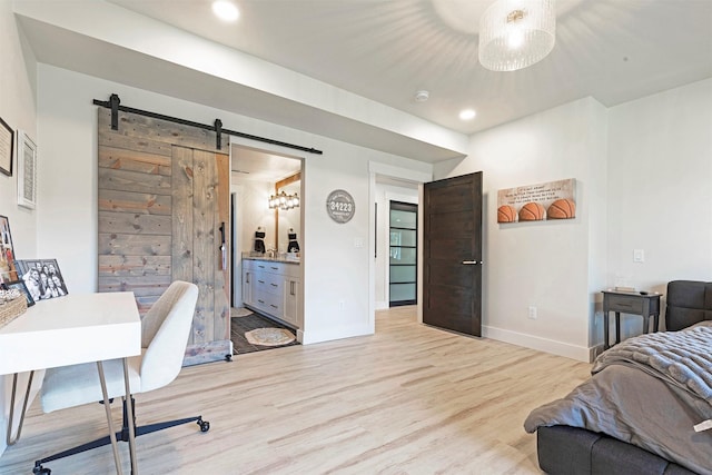 bedroom with a barn door, light hardwood / wood-style floors, and connected bathroom