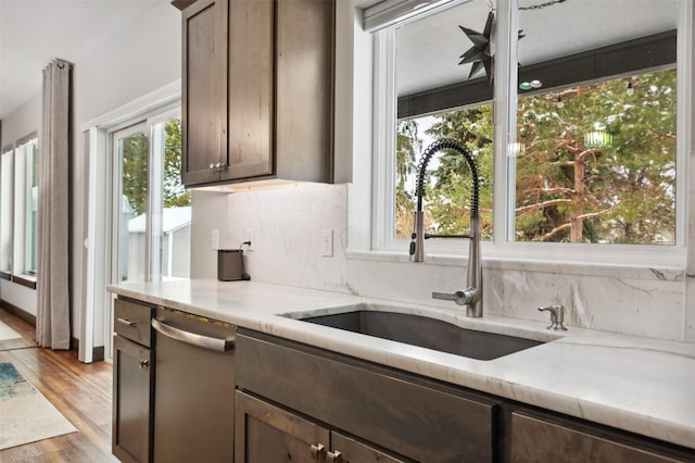 kitchen featuring sink, light hardwood / wood-style flooring, stainless steel dishwasher, dark brown cabinets, and light stone counters