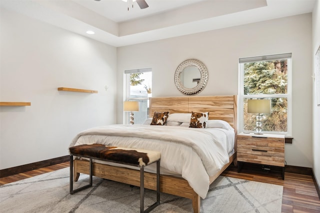 bedroom with hardwood / wood-style flooring, a raised ceiling, and ceiling fan