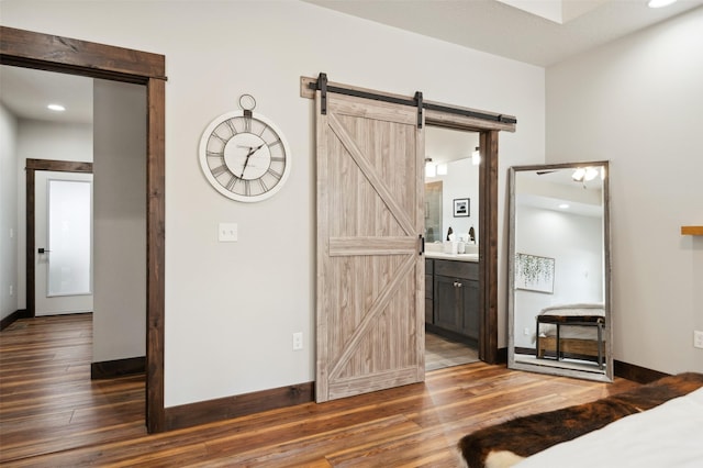 unfurnished bedroom featuring a barn door, dark hardwood / wood-style floors, and connected bathroom