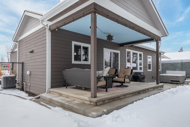 snow covered back of property with central AC unit and a hot tub