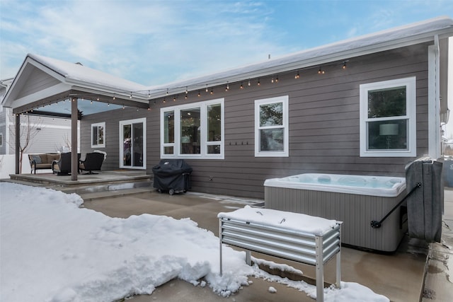 snow covered house featuring a patio and a hot tub