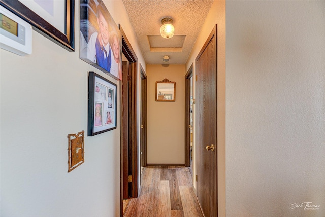 hall with a textured ceiling, light hardwood / wood-style flooring, and a raised ceiling