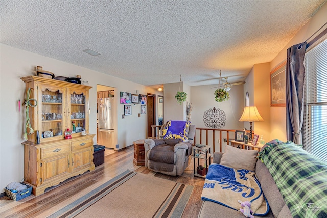 living room featuring wood-type flooring, a textured ceiling, and ceiling fan