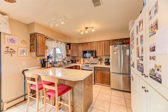 kitchen with a textured ceiling, appliances with stainless steel finishes, a baseboard radiator, kitchen peninsula, and a breakfast bar area