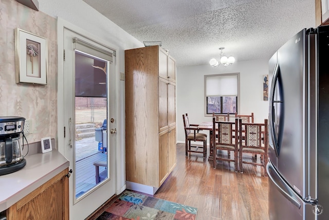 kitchen featuring decorative light fixtures, an inviting chandelier, a textured ceiling, light wood-type flooring, and stainless steel refrigerator