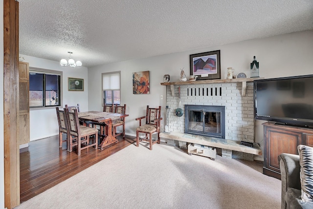 living room with a textured ceiling, a notable chandelier, a brick fireplace, and dark colored carpet