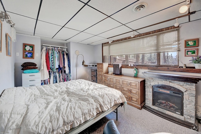 carpeted bedroom featuring a drop ceiling, a closet, and a stone fireplace