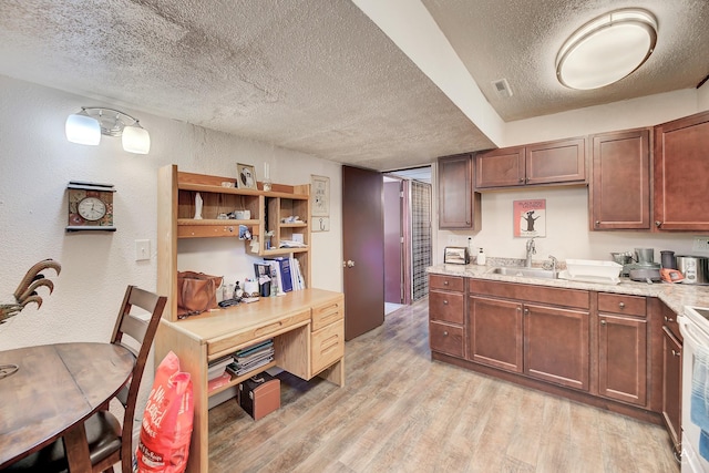 kitchen featuring sink, a textured ceiling, light wood-type flooring, and light stone countertops