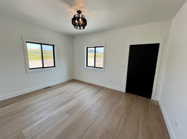 empty room featuring a healthy amount of sunlight, light wood finished floors, baseboards, and visible vents